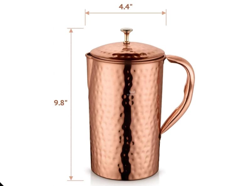 May include: A copper pitcher with a hammered texture, a lid, and a curved handle. The pitcher is 9.8 inches tall and 4.4 inches wide. The pitcher has a shiny, metallic finish and is designed for serving beverages.