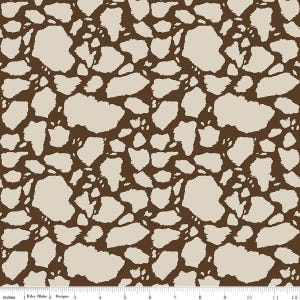 May include: A fabric pattern featuring an irregular, organic giraffe-like spot design in dark brown and light beige. A white ruler at the bottom edge displays measurements in inches, with the text Riley Blake Designs printed on the left side.