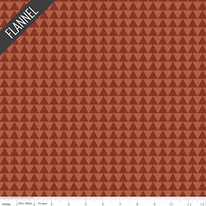 May include: A fabric with a repeating pattern of brown triangles. The word "FLANNEL" is printed on a diagonal black banner in the upper left corner. The bottom of the image has a ruler with inches.