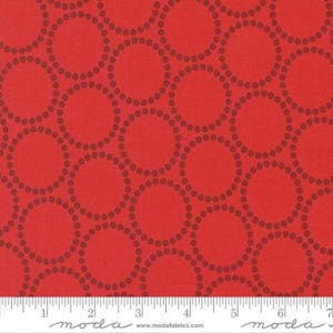 May include: Red fabric with a repeating pattern of dark red circles outlined with small dots. The fabric has a textured appearance. A ruler is at the bottom of the image, with the word "moda" printed on it.