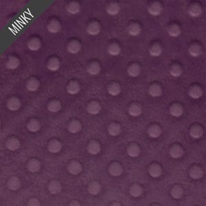 May include: Close-up of a plush, deep purple minky fabric with a raised dot pattern. The fabric has a soft, velvety texture. The word "MINKY" is printed on a diagonal black label in the upper left corner.