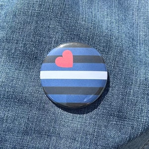 May include: A blue and black striped button with a white stripe and a red heart in the center.