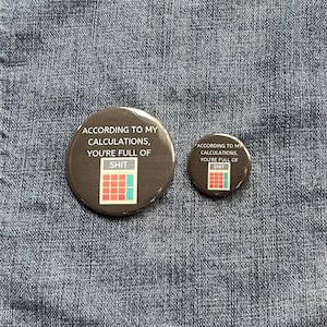 May include: Two round, dark brown buttons with the text "ACCORDING TO MY CALCULATIONS, YOU'RE FULL OF SHIT" and a calculator graphic. One button is larger than the other. The buttons are on a blue denim background.