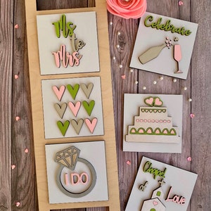 May include: A wooden ladder with five square signs attached to it. The signs are decorated with wedding-themed designs, including the words "Mrs. to Mrs.", hearts, a ring with the words "I Do", a cake, and a church with the words "Chapel of Love".