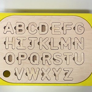 May include: A yellow wooden alphabet puzzle with all the letters of the alphabet cut out. The letters are in a grid pattern and are easy to remove and replace.