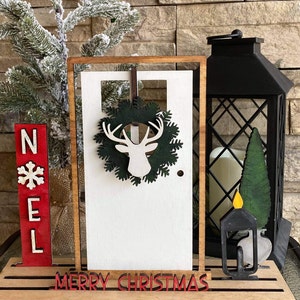May include: Wooden Christmas decor with a white door, a green wreath with a deer silhouette, a red "NOEL" sign, and a black lantern with a candle.