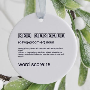 May include: White ceramic ornament with the word "DOG GROOMER" spelled out in black letters with a definition and the text "word score: 15".