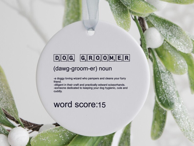 May include: White ceramic ornament with the word "DOG GROOMER" spelled out in black letters with a definition and the text "word score: 15".