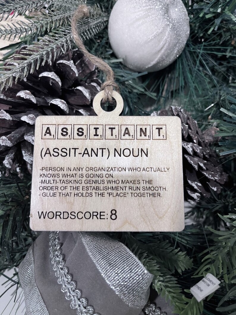 May include: Wooden Christmas ornament with the word "ASSISTANT" spelled out in Scrabble tiles. The ornament also includes the definition of the word, "Person in any organization who actually knows what is going on. Multi-tasking genius who makes the order of the establishment run smooth. Glue that holds the "place" together." and the wordscore, "WORDSCORE: 8".