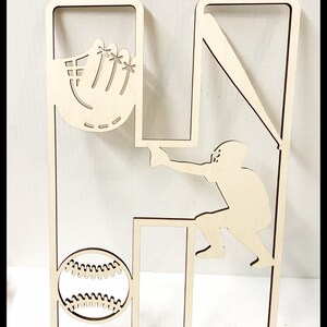May include: Wooden cutout of the letter H with a baseball player, bat, glove, and baseball inside the letter.
