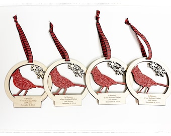 May include: Four wooden Christmas ornaments with red glitter cardinal birds and snowflakes. Each ornament has a red and black plaid ribbon and a personalized message that reads "In Memory of our Husband Father and Nonno December 9, 2014".