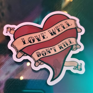 以下が含まれることがあります： 白い輪郭と「Love Well Don't Kill」と書かれたバナーが付いた赤いハート。ハートは白い輪郭と「Love Well Don't Kill」と書かれたバナーで囲まれています。