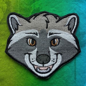 May include: Embroidered patch featuring a smiling raccoon face with gray, white, and black details. The patch has a black border and brown eyes. The background is a gradient of green and blue. The text "PantheraPalm" is at the bottom.