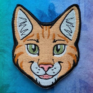 May include: Embroidered patch of a smiling cat's face, with orange and tan fur, green eyes, and a pink nose and mouth. The patch has a black border and is on a tie-dye background. The logo "Panthera Palm" is in the lower left corner.
