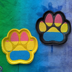 Puede incluir: Dos parches bordados con huellas de pata. Uno es amarillo con detalles rosas y azules, el otro es negro con detalles rosas, amarillos y azules. Los parches están sobre un fondo colorido con el texto "PantheraPalm".