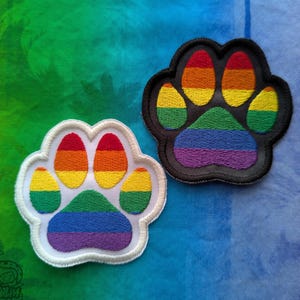 Puede incluir: Dos parches con forma de huella de pata de arcoíris. Uno es blanco con bordado de arcoíris y el otro es negro con bordado de arcoíris.
