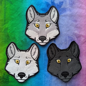 May include: Three embroidered wolf head patches. The wolf heads are grey, white, and black. Each wolf has yellow eyes and a black nose.