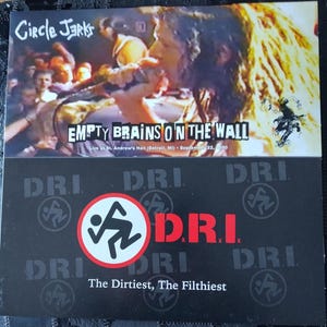 May include: A black and white album cover featuring the band DRI. The top half displays a live performance image with the text "EMPTY BRAINS ON THE WALL." The bottom half has the DRI logo and the text "The Dirtiest, The Filthiest."
