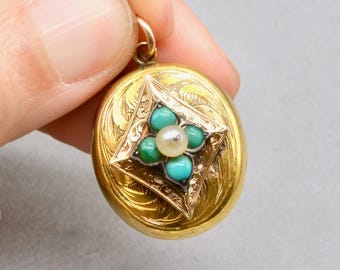 Peut inclure: Un médaillon rond de couleur or avec un motif floral gravé. Le médaillon présente un carré central avec un motif de fleur composé de pierres turquoise et vertes, avec une perle au centre. Le médaillon est tenu par une main.