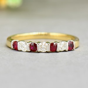 Puede incluir: Un anillo de banda de oro con rubíes rojos y diamantes blancos alternados. El anillo está engastado en una banda de oro amarillo con un acabado pulido.