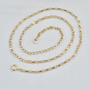 May include: A delicate gold-colored chain necklace with a repeating oval link design. The necklace is displayed on a light gray surface, with a clasp at one end and a small ring at the other. The chain is a simple, elegant piece of jewelry.