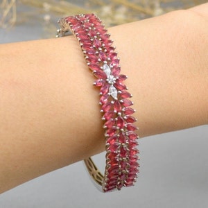 May include: A silver bangle bracelet with a double row of pink marquise-shaped gemstones and a cluster of white round gemstones in the center.