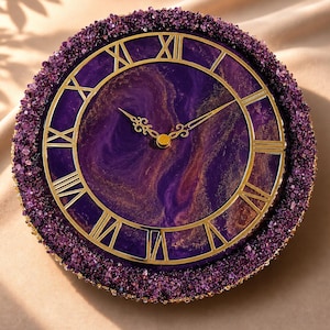 May include: A round wall clock featuring a deep purple and gold marbled face with gold Roman numerals and ornate gold hands. The outer edge of the clock is decorated with a thick border of small, textured, dark purple crystalline stones.