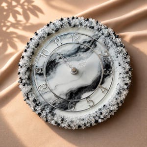 May include: A round wall clock featuring a white and black marbled face with silver-toned numerals and hands. The outer edge is heavily embellished with a dense border of small, clear and black faceted beads, creating a textured, sparkling frame.