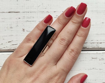 May include: A black rectangular ring with a silver band. The ring is worn on the index finger of a hand with red nail polish.