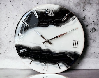 May include: A round wall clock with a white and black marbled design. The clock face features silver Roman numerals and hands. The clock's design has a modern aesthetic.