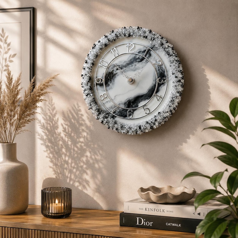 May include: A round wall clock featuring a white and black marbled face with silver-toned numerals. The outer edge is decorated with a dense border of small, clear, and black beads. The clock has thin silver hands and a circular silver frame.