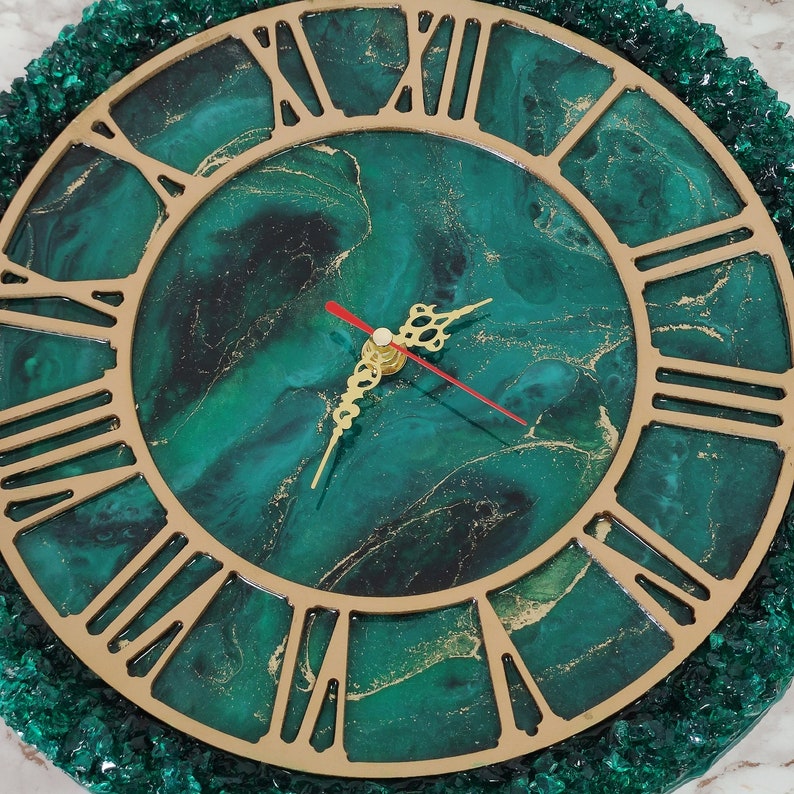 May include: A circular wall clock featuring a green and gold marbled design with gold Roman numerals. The clock hands are gold with a red second hand. The clock is framed by a border of green crystals. A decorative item for the home.