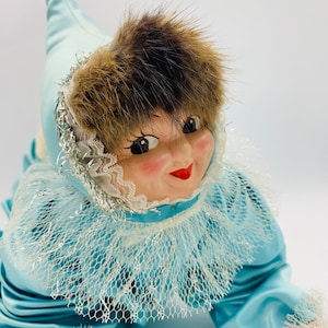 May include: A vintage doll with a blue and white dress, a fur hat, and a painted face. The doll has rosy cheeks and red lips.