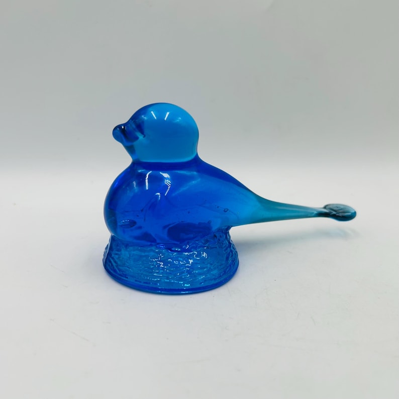 Puede incluir: Una vibrante figura de p&aacute;jaro de cristal azul. El p&aacute;jaro tiene un cuerpo redondeado, una cabeza peque&ntilde;a y una cola larga y puntiaguda. La base del p&aacute;jaro es texturizada. La figura est&aacute; hecha de vidrio transparente, permitiendo el paso de la luz.