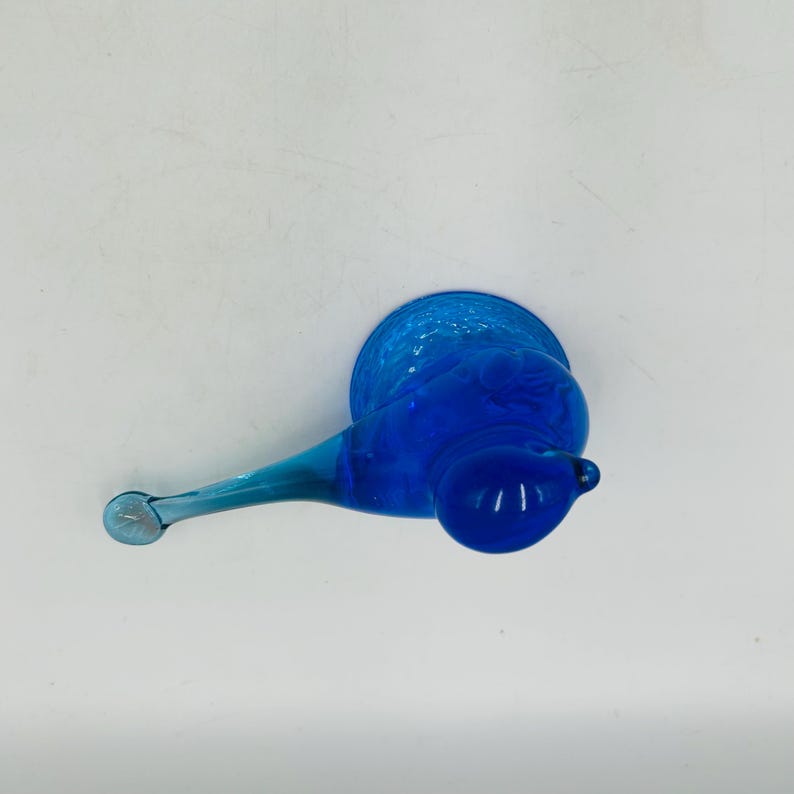 Puede incluir: Un objeto de vidrio azul vibrante con un cuerpo bulboso y un mango delgado y alargado. El vidrio tiene un acabado liso y brillante, y el color es un azul profundo y saturado. El objeto parece ser una pieza decorativa o una creaci&oacute;n de arte en vidrio &uacute;nica.