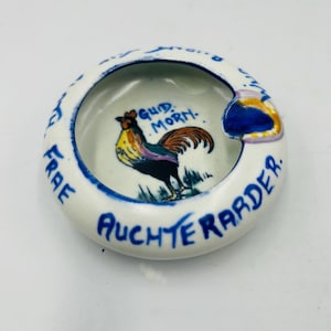 May include: White ceramic ashtray with a blue rim and the words "Auchterarder" and "Frae" in blue. The center features a colorful rooster illustration and the words "Gud Morn."