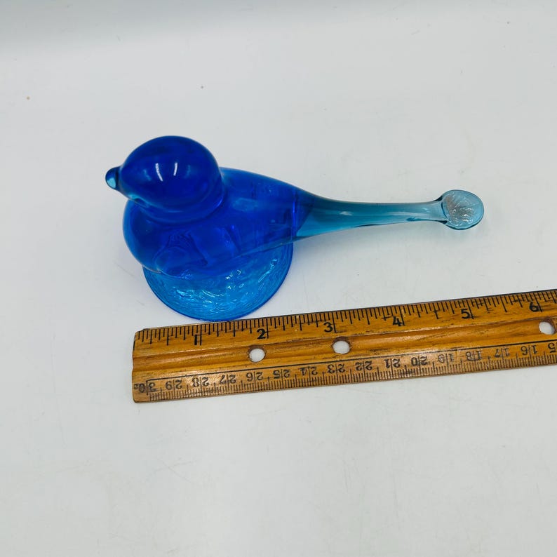 Puede incluir: Una figura de p&aacute;jaro de cristal azul vibrante. El p&aacute;jaro tiene un cuerpo redondeado y una cola larga y delgada. La figura mide aproximadamente 13 cm de largo, con una base texturizada. El p&aacute;jaro es un art&iacute;culo decorativo.