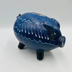 May include: A blue ceramic piggy bank with white and gold accents. The piggy bank has a wavy design and three legs.