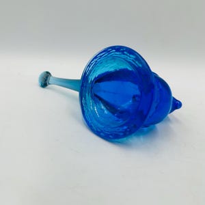 Puede incluir: Una vibrante flor de cristal azul con un largo tallo y una cabeza acampanada y texturizada. El dise&ntilde;o de la flor presenta una forma bulbosa en el lateral. El cristal tiene un acabado brillante, que refleja la luz. Este art&iacute;culo decorativo podr&iacute;a usarse como jarr&oacute;n o una pieza de arte &uacute;nica.