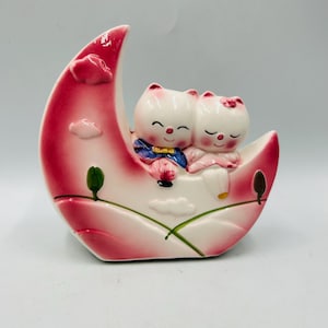 vintage kitschy anthropomorphic cat couple sitting on a pink moon bank