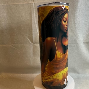 May include: A stainless steel tumbler featuring a portrait of a woman with dark hair and a yellow dress. The artwork has a warm color palette with gold and brown tones. The tumbler has a black base and a silver lid.