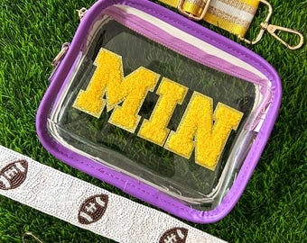 May include: Clear stadium-approved bag with purple trim and gold hardware. The bag features the letters "MIN" in gold, with a yellow and white striped strap, a solid purple strap, and a white strap with football designs.