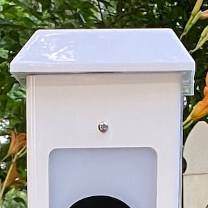 May include: White plastic birdhouse with a peaked roof and a small opening for birds to enter. The birdhouse is mounted on a white post.