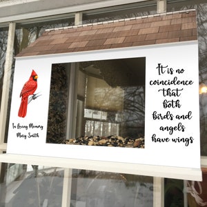 May include: A white bird feeder with a red cardinal perched on a branch. The feeder has a clear window and is filled with birdseed. The feeder is mounted on a window and has a sign that reads "It is no coincidence that both birds and angels have wings."  The sign also includes the text "In loving memory Mary Smith".