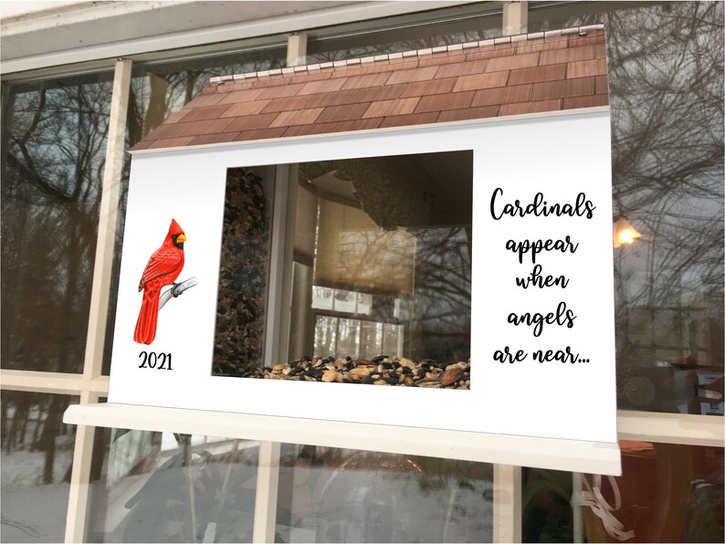 May include: A white bird feeder with a red cardinal perched on a branch. The feeder has a brown roof and a clear window. The text "Cardinals appear when angels are near..." is printed on the feeder. The year 2021 is printed on the bottom left corner of the feeder.
