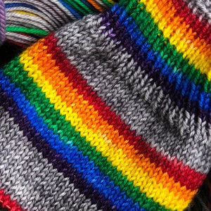 May include: Close-up of a knitted fabric with a rainbow stripe pattern. The fabric is gray with stripes of red, orange, yellow, green, blue, indigo, and violet.