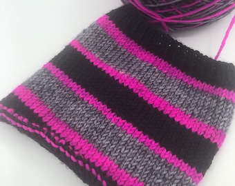 May include: A close-up of a knitted fabric swatch with black, gray, and pink stripes. The fabric is knit in a simple stitch and has a slightly textured surface.