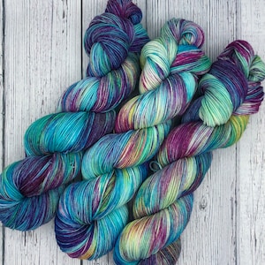 May include: Three skeins of yarn in a variegated colorway with shades of teal, purple, green, and yellow.