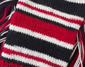 May include: A knitted scarf with red, white, and black stripes. The scarf has a fringe on both ends.