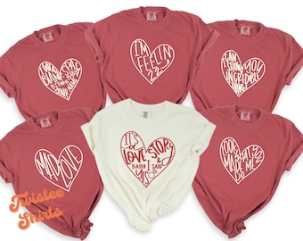 Op de afbeelding: Zes rode T-shirts met witte hartontwerpen. De shirts bevatten verschillende spreuken in de harten, waaronder "I'm feelin' 22", "I can show you incredible things", "Mad Love", "It's a love story & baby I said yes", en "Look what you made me do".
